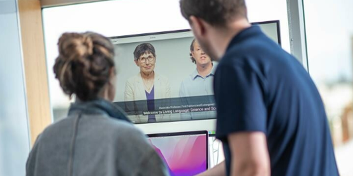 Two employees facing away from camera looking at video with captions on computer screen