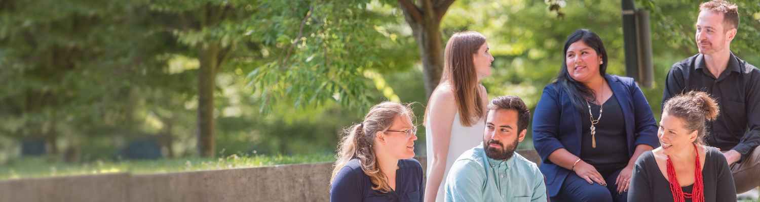 six people sitting outdoors smiling at each other.