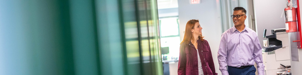 Two professionals walking indoors and smiling.