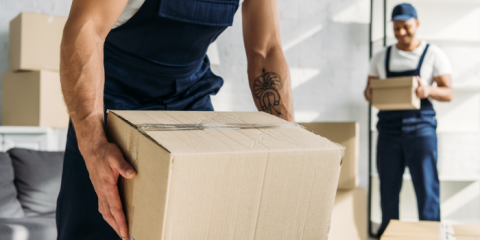 One mover carrying a box in the foreground, another in the background holding another box