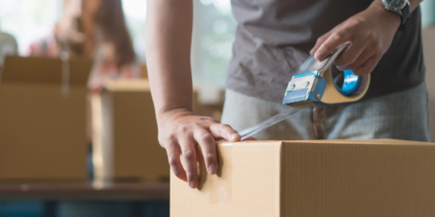 Close up of a person's hands closing a moving box using tape