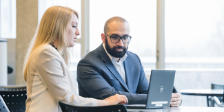 Man and woman in professional setting sitting in office and looking at a laptop